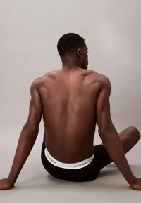 Calvin Klein black boxer briefs, seated rear model view