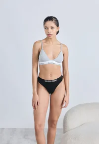 Model wearing black Calvin Klein thong, full-length front view