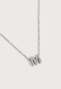 Close-up of the silver-coloured letter M pendant
